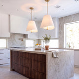 A modern kitchen with two Jada Large Conical Pendants in Modern Brass with white shades over a marble waterfall island and dark wood cabinets.
