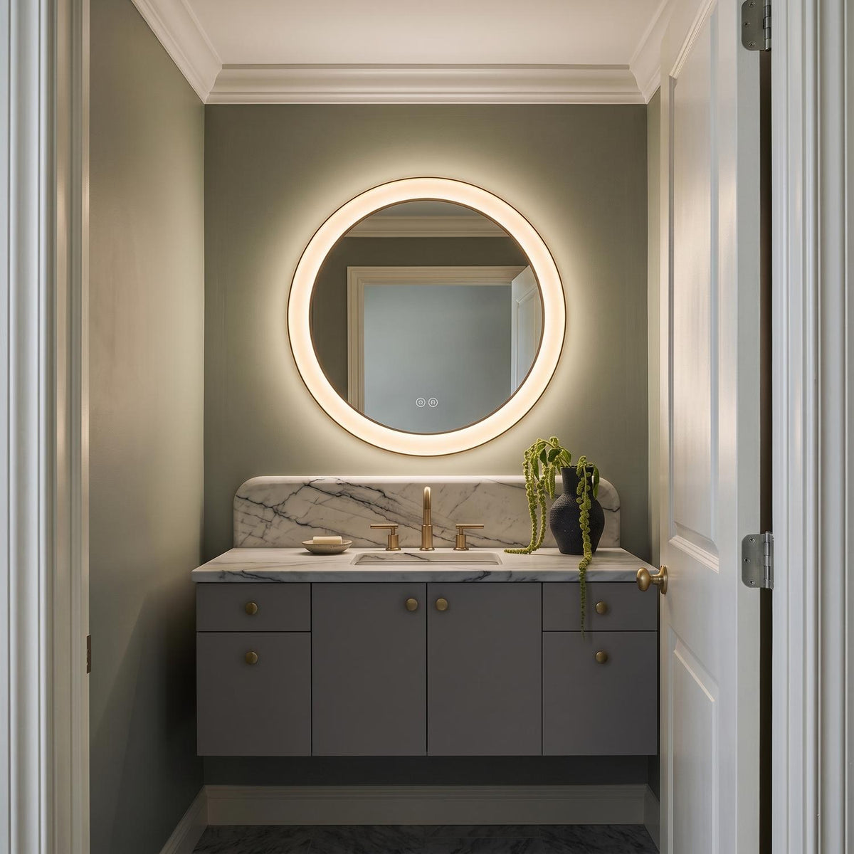 A contemporary bathroom with a Hedley Round LED Mirror 24" x 24", Modern Brass above a white marble countertop and gray floating cabinet against sage green walls.