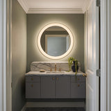 A contemporary bathroom with a Hedley Round LED Mirror 24" x 24", Modern Brass above a white marble countertop and gray floating cabinet against sage green walls.
