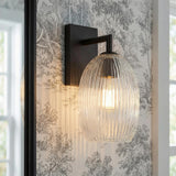 Fiora Wall Sconce 10", Matte Black linear glass Wall Sconce in a Traditional Bathroom with toile wallpaper and a black framed mirror.