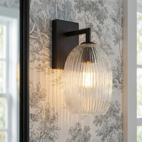 Fiora Wall Sconce 10", Matte Black linear glass Wall Sconce in a Traditional Bathroom with toile wallpaper and a black framed mirror.