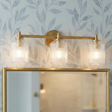 Lathan 3 Light Vanity 26", Modern Brass linear glass Vanity in a Transitional Bathroom with leaf wallpaper and a gold mirror.