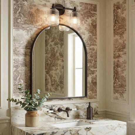 A traditional bathroom featuring a two light vanity in aged iron with ribbed glass shades mounted over an arched mirror and veined marble countertop.