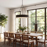 A transitional dining room featuring a Bishop Ring Chandelier 36 inch in aged iron over a light wood table with cane chairs on a textured rug.