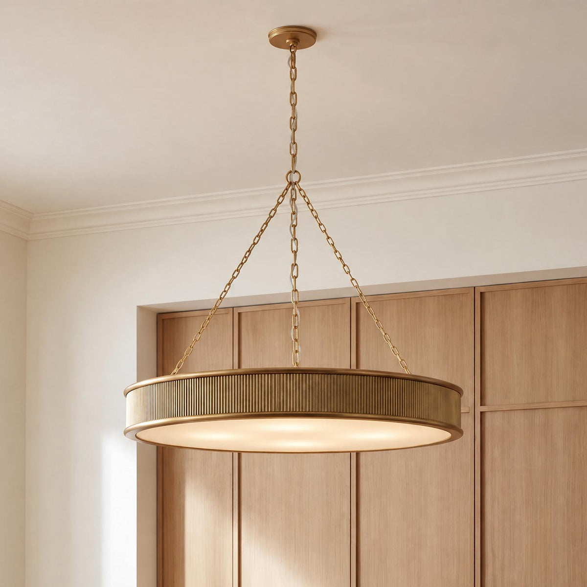 A transitional living room featuring the Bishop Ring Chandelier 36", Gilded Brass with ribbed brass trim and frosted glass suspended in front of light wood paneling.