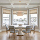 A coastal dining room features the Daria Large Pendant 26", Gilded Brass and White over a pedestal table under a coffered ceiling with bay window harbor views.