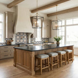 A transitional kitchen with two Cambria Large Lantern Pendant 21", Matte Black and Modern Brass fixtures over a wood island and patterned backsplash under a beamed ceiling.