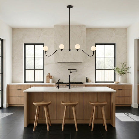 A contemporary kitchen features the Leora 4 Light Linear Pendant 48", Matte Black with frosted glass globes over a white marble island and fluted wood cabinets.
