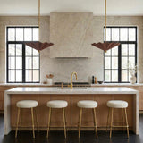 A contemporary kitchen features two Babette Large LED Pendant 25", Maroon and Brass fixtures flanking a stone range hood above a fluted wood island with four stools.