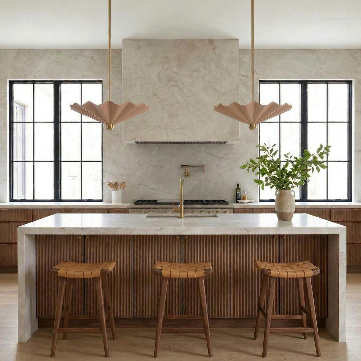 A contemporary kitchen features two Babette Large LED pendants in blush and brass over a white marble waterfall island with fluted wood cabinetry and black windows.