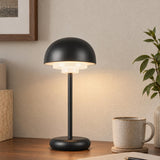A mid-century modern office with the black Carola Rechargeable Table Lamp on a dark wood desk next to a speckled ceramic coffee mug and potted greenery.