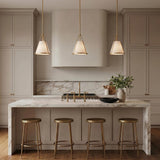 A contemporary kitchen with three Hoyt Small Conical Pendant 9" Antique Gold fixtures over a marble waterfall island with gold counter stools and beige cabinetry.