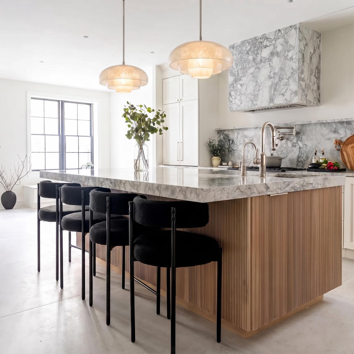 A modern kitchen with two Jalina Pendant 18-inch Polished Nickel and Art Glass fixtures hanging over a marble-topped fluted wood island beside a matching marble range hood.