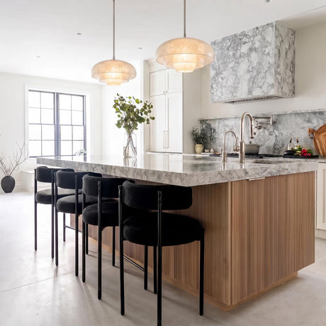 A modern kitchen with two Jalina Pendant 18-inch Polished Nickel and Art Glass fixtures hanging over a marble-topped fluted wood island beside a matching marble range hood.