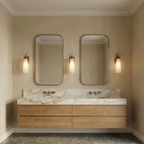 A modern bathroom featuring the Vox Wall Sconce 15", Patina Brass with frosted glass, flanking mirrors above a marble countertop and floating wood double vanity.