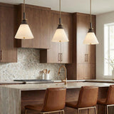 A mid-century kitchen features three Armon Medium Pendant 16 inch Opal Glass with Bronze and Patina Brass fixtures hanging over a marble island with a hexagon backsplash.