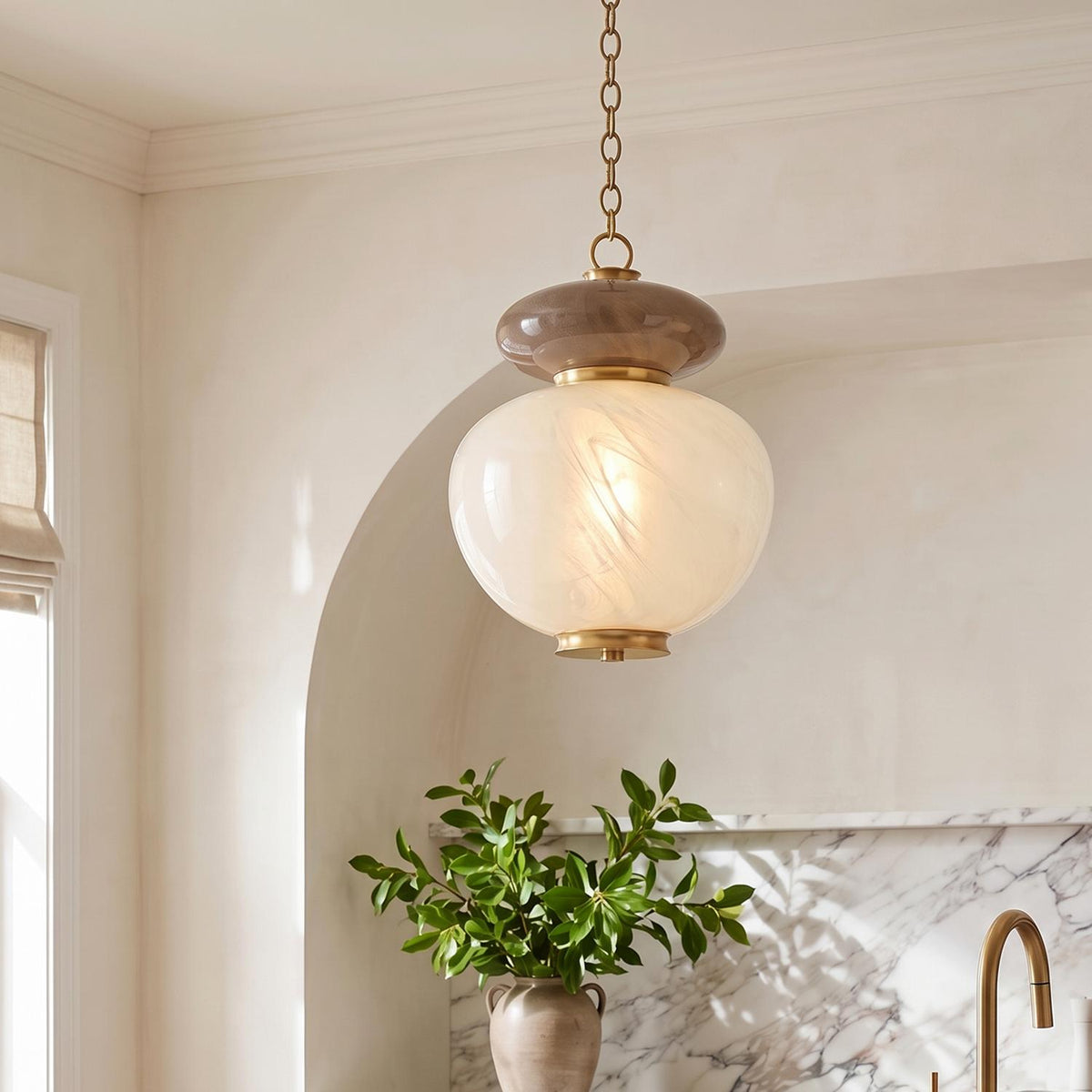 A transitional kitchen features the Danara Medium LED Pendant in two-tone art glass and brass hanging above a marble countertop with a brass faucet.