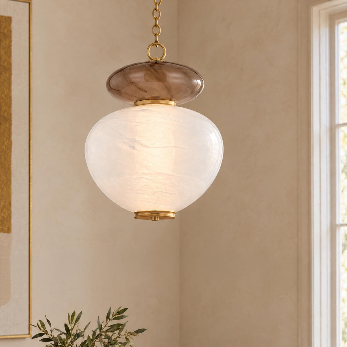 A transitional living room featuring the Danara Large LED Pendant 19", Two-Tone Art Glass and Brass suspended near a window with warm plaster walls and framed art.
