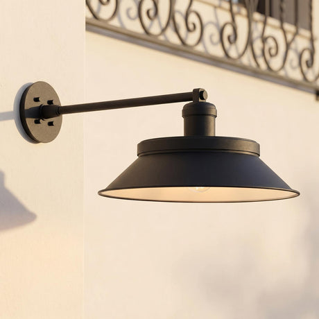 A Mediterranean patio with the Vinya Outdoor Wall Light, Large, Matte Black barn light mounted on white stucco beside a decorative wrought iron railing.
