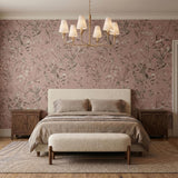 A traditional bedroom with the Junia 6 Light Chandelier in a textured gold finish and white linen shades centered over a cream upholstered bed against pink floral wallpaper.