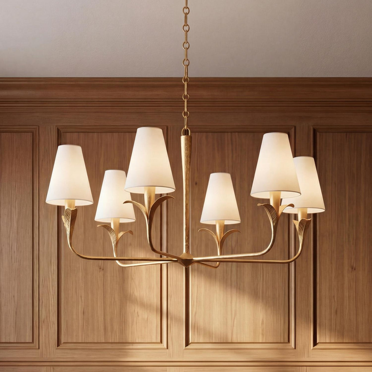 A traditional dining room featuring the Junia 6 light chandelier in textured gold with white linen shades suspended in front of natural wood wall paneling.