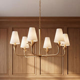 A traditional dining room featuring the Junia 6 light chandelier in textured gold with white linen shades suspended in front of natural wood wall paneling.