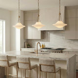 A transitional kitchen features three Balina Medium Pendant 14 inch, Patina Brass and Milk Glass fixtures suspended over a marble waterfall island and beige flat-panel cabinetry.