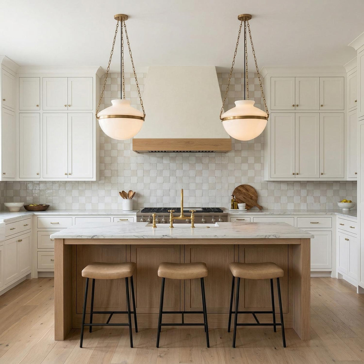 A transitional kitchen features two Capella Large Pendant 19", Patina Brass and Milk Glass over a white marble island with a light wood base and checkerboard tile backsplash.