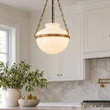 A transitional kitchen features the Capella Large Pendant in Patina Brass and Milk Glass hanging over a marble counter near white cabinets and a marble backsplash.
