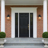 A Colonial red brick entrance with two Baelor Outdoor Wall Lights in textured black flanking a black front door at dusk featuring boxwood shrubs and stone steps.