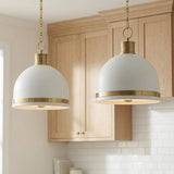 A transitional kitchen features two Patrice Medium Pendant 15", Matte White and Aged Brass fixtures over the island alongside light wood cabinets and white subway tile backsplash.