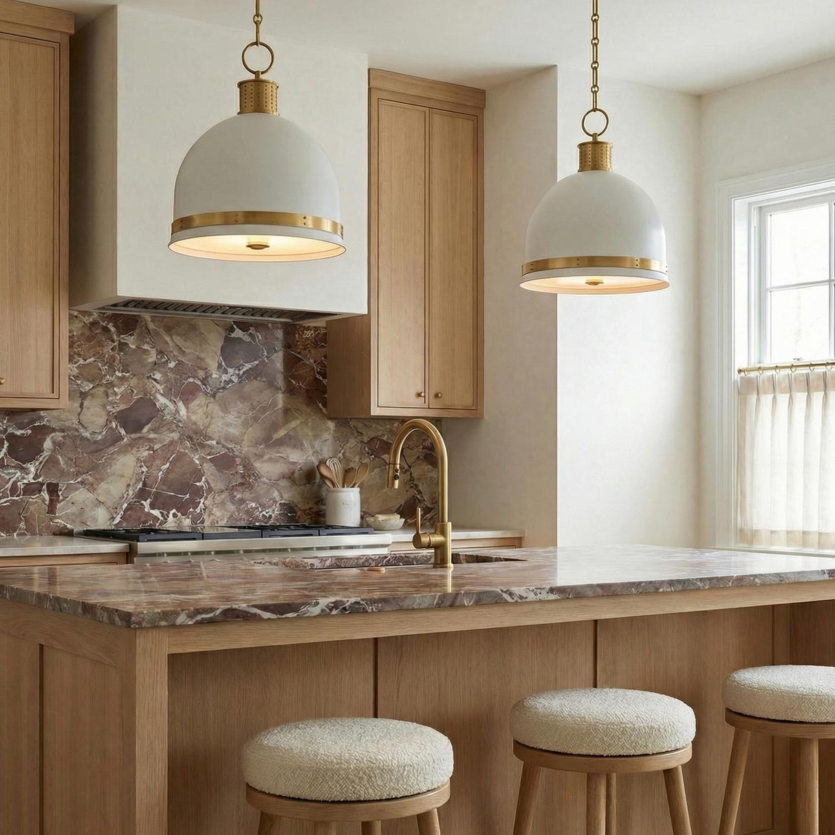 A transitional kitchen features two Patrice Medium Pendant 15", Matte White and Aged Brass fixtures hanging over a wood island with brown marble countertops and light cabinets.