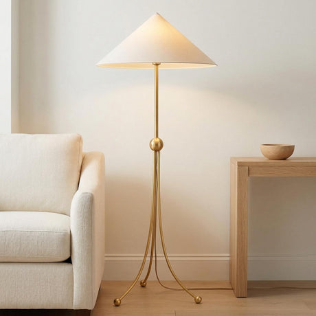 A contemporary living room featuring the Ivana Floor Lamp 61", Aged Brass with a linen cone shade standing between a beige sofa and a light wood table.