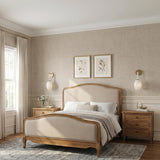 A traditional bedroom with two Helena Wall Sconce 15" fixtures in aged brass and cloud glass flanking an upholstered bed set against tan grasscloth wallpaper.