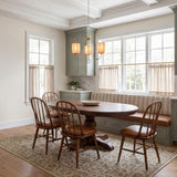 A traditional dining room featuring an aged brass chandelier with fabric shades suspended over a dark wood pedestal table and sage green cabinetry under a coffered ceiling.