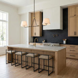 A transitional kitchen features the Eamon 2 Shade Linear Pendant in distressed bronze and aged brass with linen shades over a marble island and black stone backsplash.