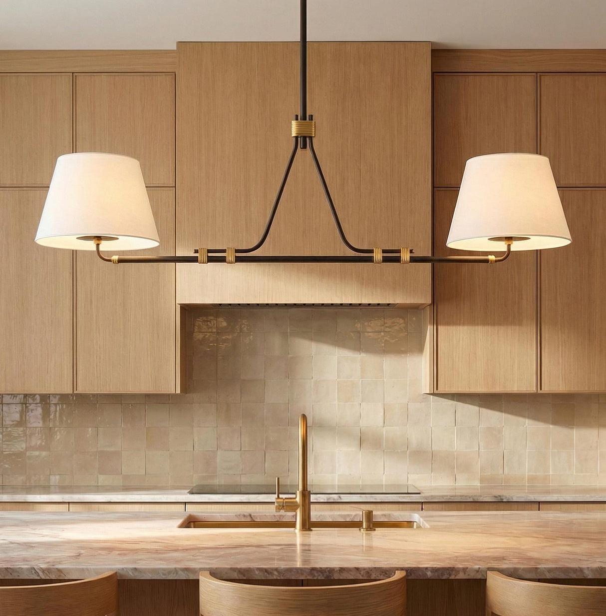 A transitional kitchen features the Eamon 2 Shade Linear Pendant 52", Distressed Bronze and Aged Brass with linen shades over the island sink and light wood cabinetry.