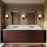 A traditional bathroom with three Eamon Wall Sconces in distressed bronze and aged brass flanking two mirrors above a burgundy vanity with a marble countertop and backsplash.