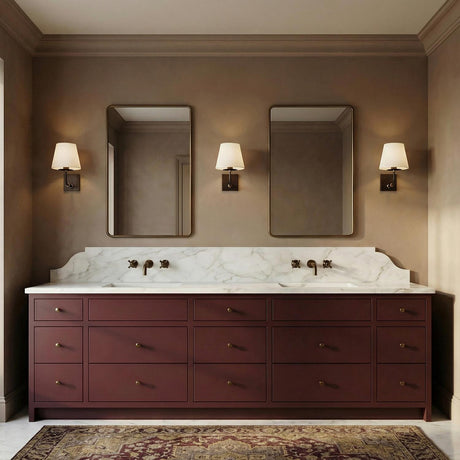 A traditional bathroom with three Eamon Wall Sconces in distressed bronze and aged brass flanking two mirrors above a burgundy vanity with a marble countertop and backsplash.