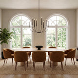 A contemporary dining room featuring an aged iron Solana 8 light chandelier over a light wood table surrounded by tan velvet chairs and arched windows.