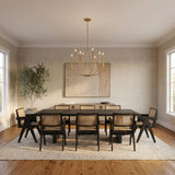 A contemporary dining room featuring the Solana 8 Light Chandelier 34" Modern Brass over a dark wood table with black cane-back chairs and hardwood floors.