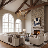 A modern farmhouse living room with the Solana 12 Light Chandelier 48-inch Modern Brass hanging from a vaulted beamed ceiling above a cream sectional and stone fireplace.
