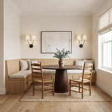A transitional dining nook featuring two Cordelia Double Wall Sconces in aged iron with white linen shades flanking artwork above a built-in wood banquette.