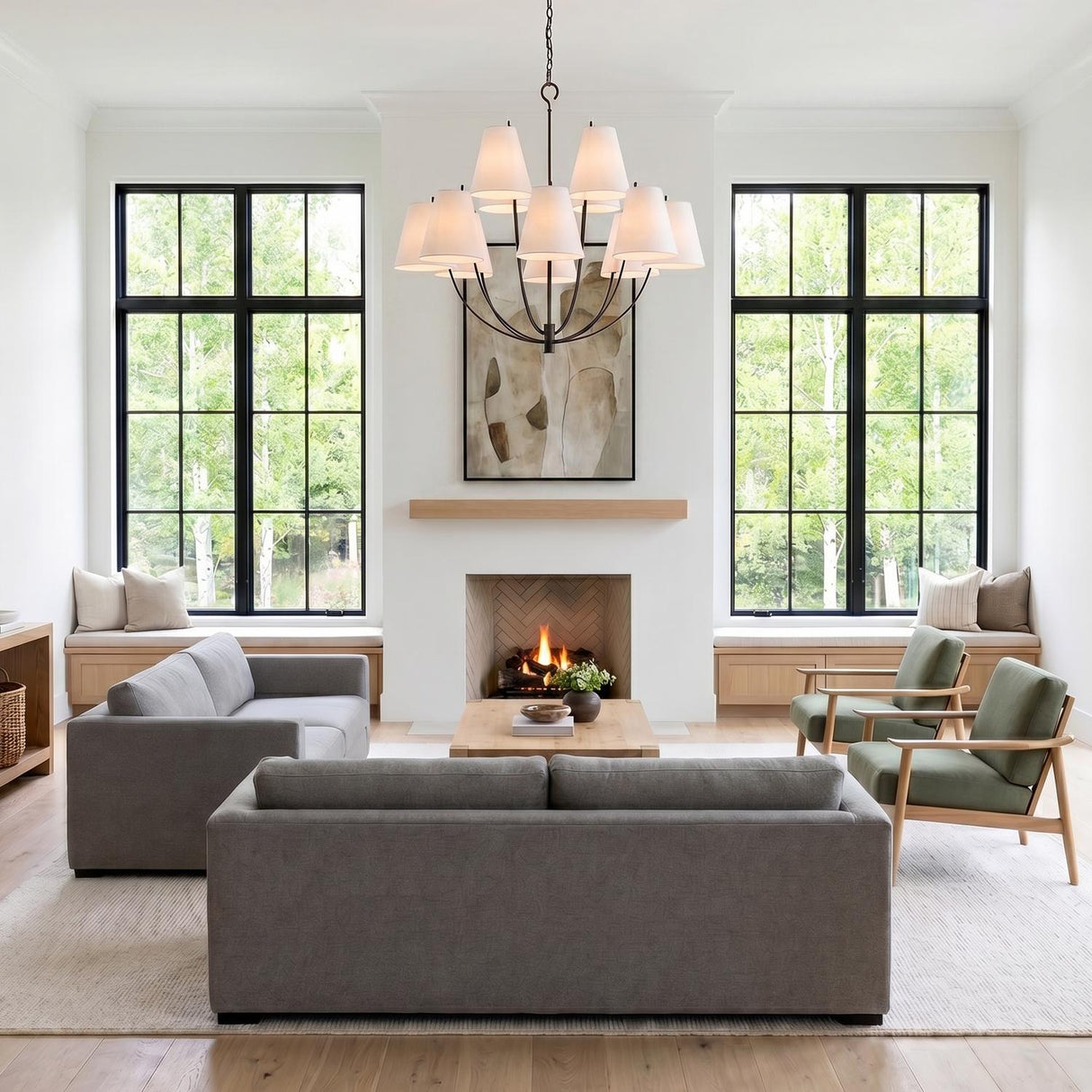 A modern farmhouse living room with the Cordelia 12 Light Chandelier 40", Aged Iron with white linen shades centered above gray sofas and a fireplace featuring herringbone tile.
