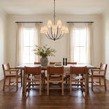 A transitional dining room featuring the Cordelia 12 Light Chandelier 40", Aged Iron with linen shades centered over a wood table and cognac leather chairs.