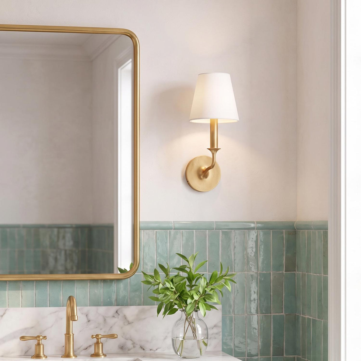A transitional bathroom features a gilded brass wall sconce with a white fabric shade mounted beside a brass mirror above seafoam green ceramic tile.