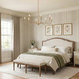 A traditional bedroom with the Harwick 8 Light Chandelier in gilded brass centered over a wood frame bed featuring striped wallpaper and framed botanical art.