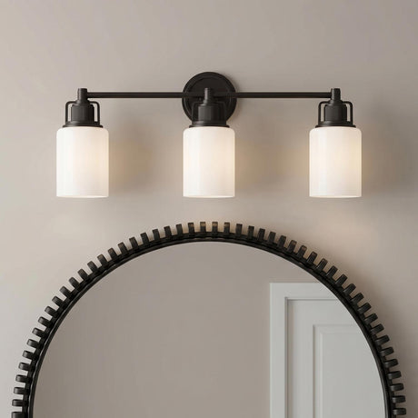 A transitional bathroom features a Claxton 3 Light Vanity 24", Aged Iron with frosted glass shades mounted over a large textured circular mirror.