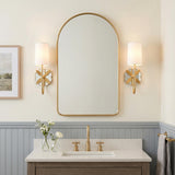 A transitional bathroom featuring two Ashby Wall Sconces in modern brass flanking an arched mirror above a white quartz vanity and blue-gray beadboard wainscoting.
