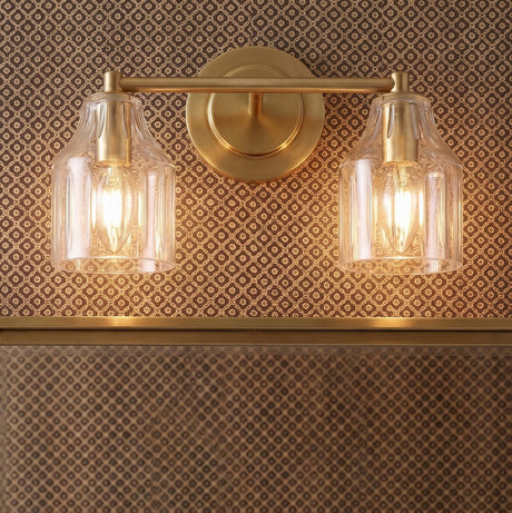 A traditional bathroom features the Radwell 2 Light Vanity 13", Gilded Brass mounted over a mirror against a brown patterned wallpaper with clear ribbed glass shades.